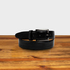 Black leather belt with a black buckle on a wooden surface