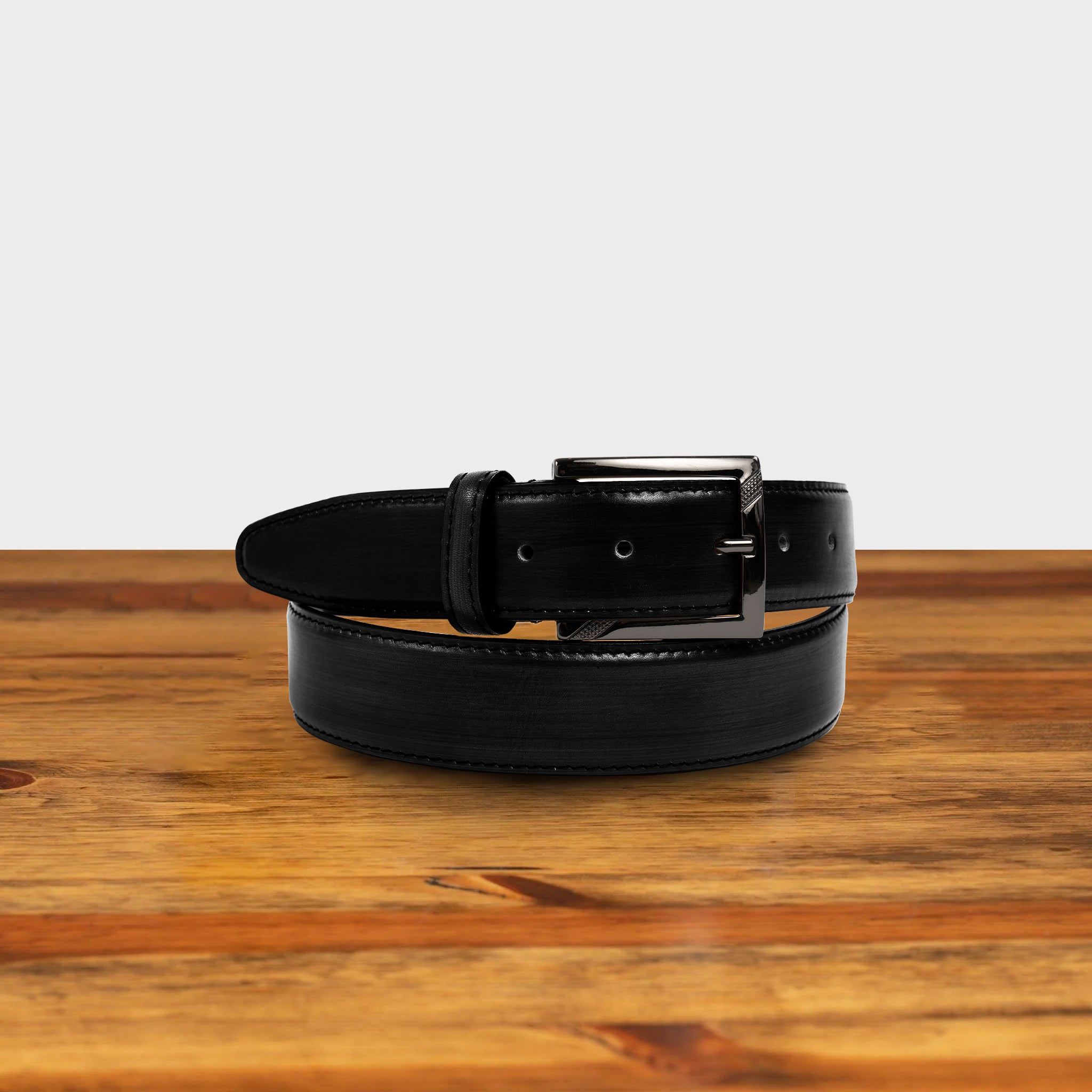 Black leather belt with a black buckle on a wooden surface