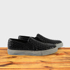 A Pair of black woven slip-on shoe on a wooden surface with a white background