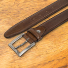 Brown leather belt with a black buckle on a wooden surface