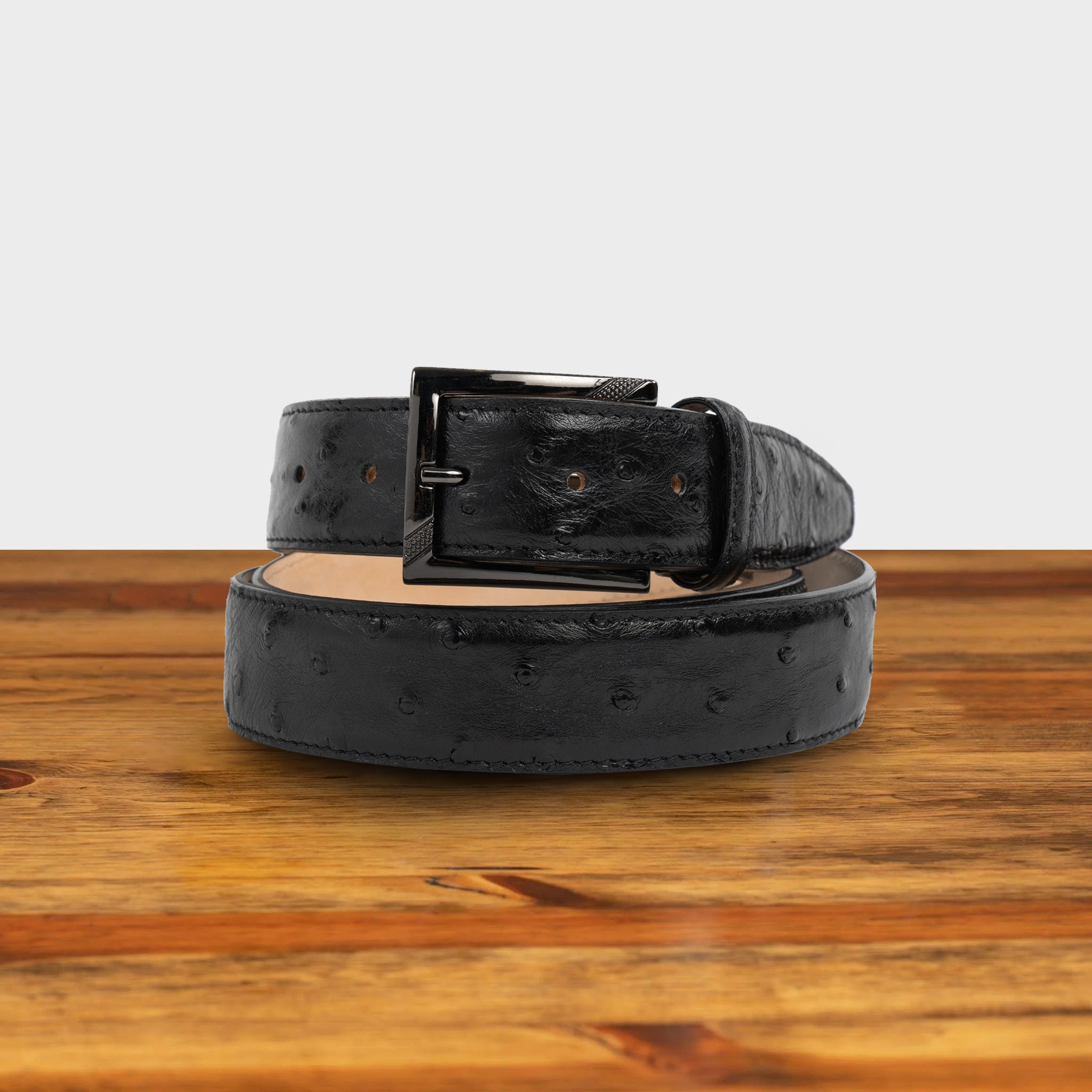 Black ostrich-patterned belt on a wooden surface with a white background