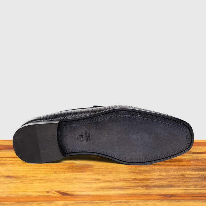 Outsole of Black leather loafer on a wooden surface with a light gray background