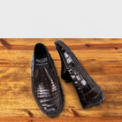 A Pair of Dark Brown crocodile-patterned loafer on a wooden surface with a light gray background