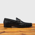 Black leather loafer on a wooden surface with a light gray background