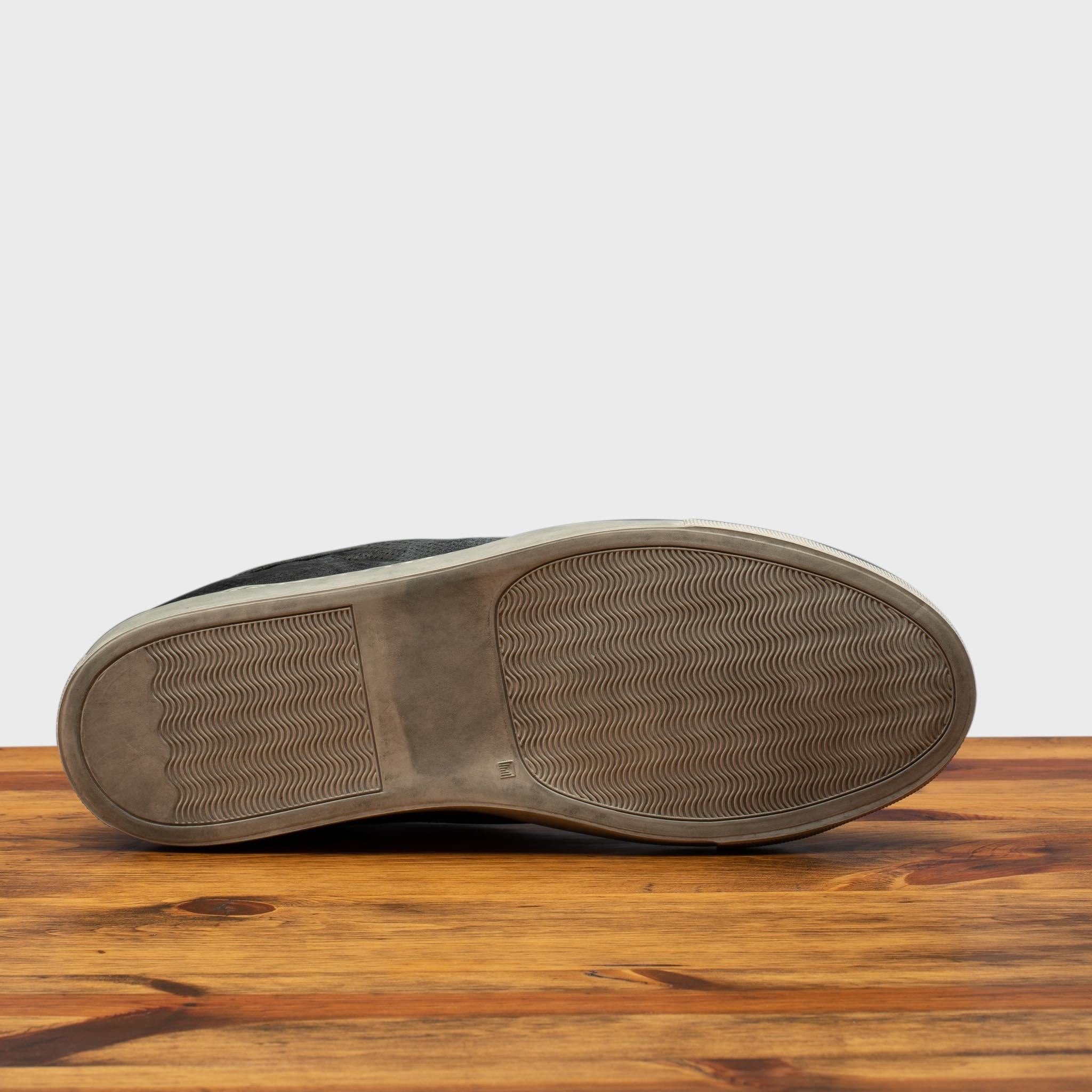 Outsole of Black sneaker on a wooden surface with a gray background