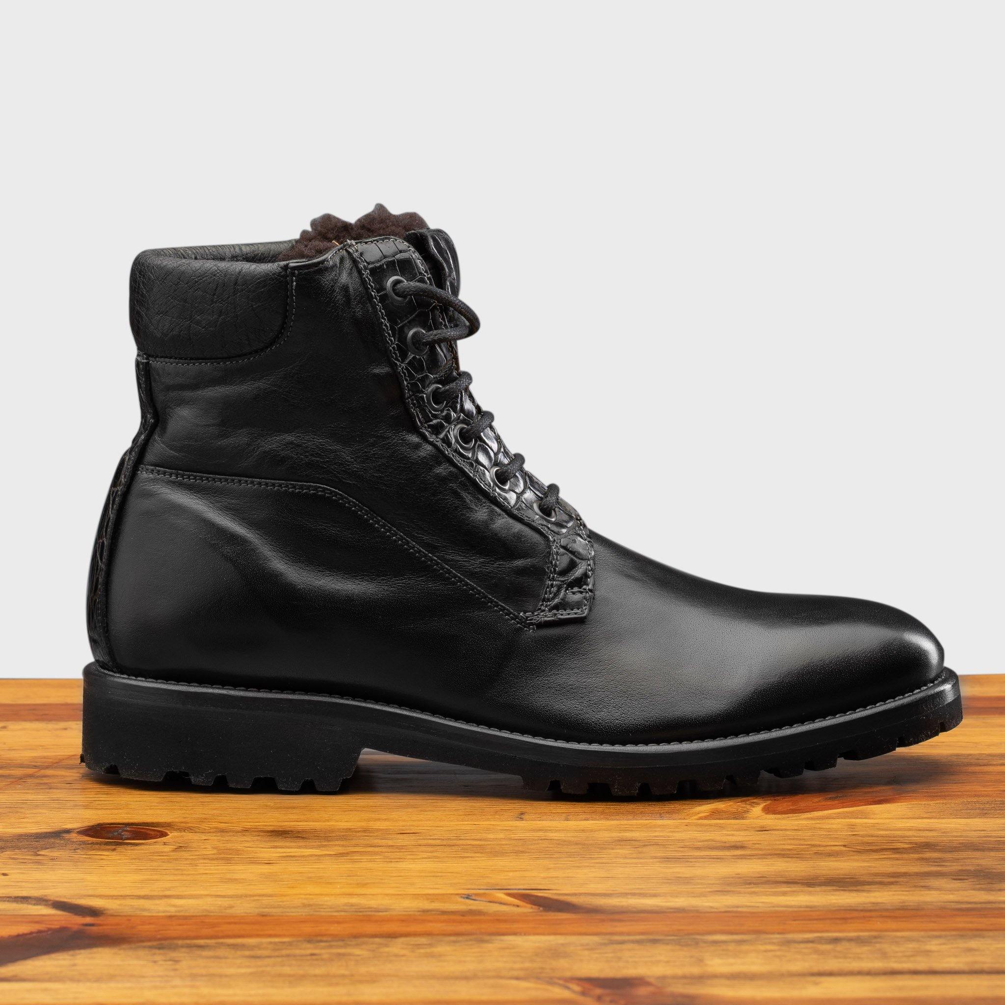 Black leather boot on a wooden surface with a light gray background