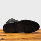 Outsole of Black leather boot on a wooden surface with a light gray background