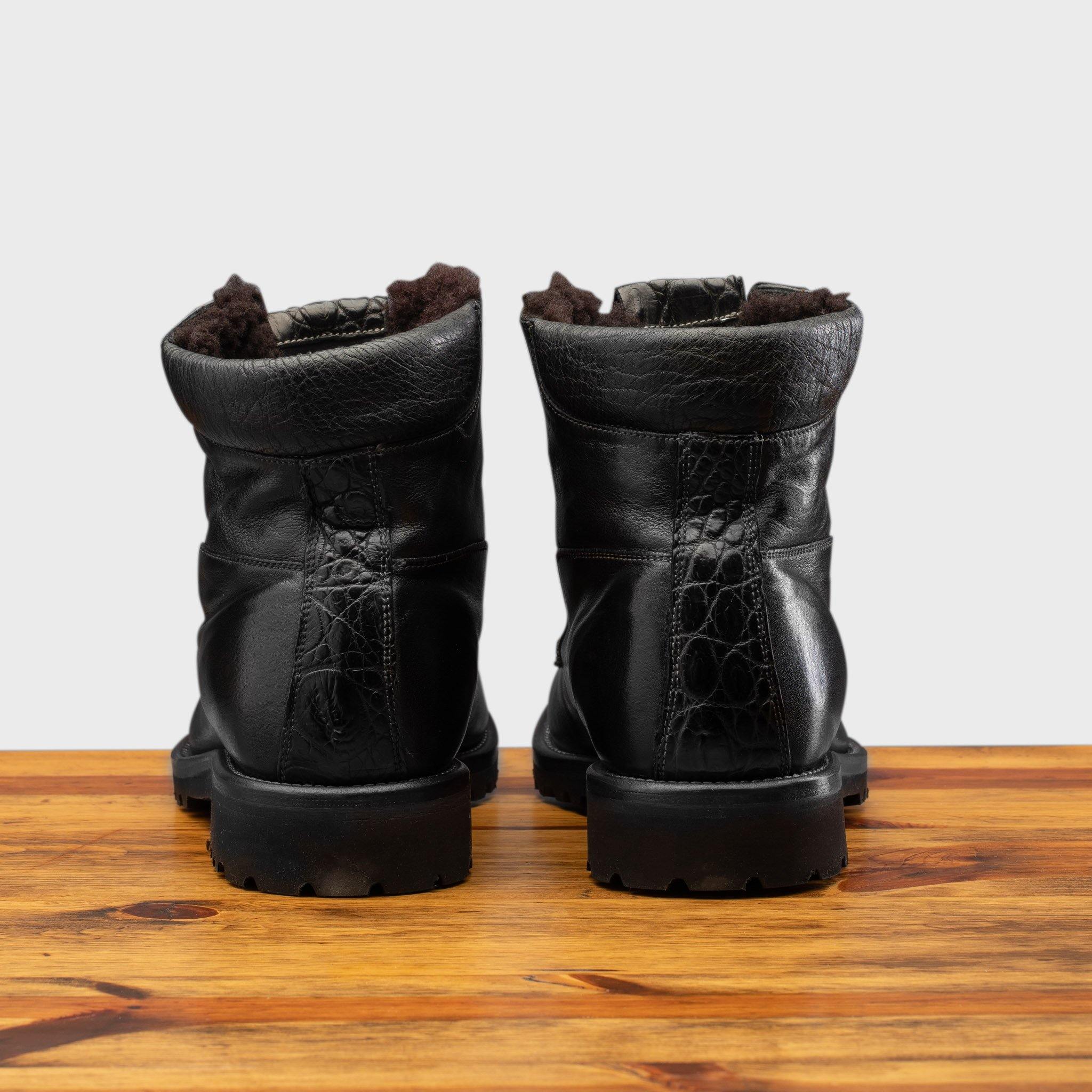 Back view of Black leather boots on a wooden surface with a light gray background