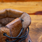 Close view of brick leather boots on a wooden surface.
