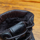 Close-up of a dark brown leather boot with shearling lining on a wooden surface.
