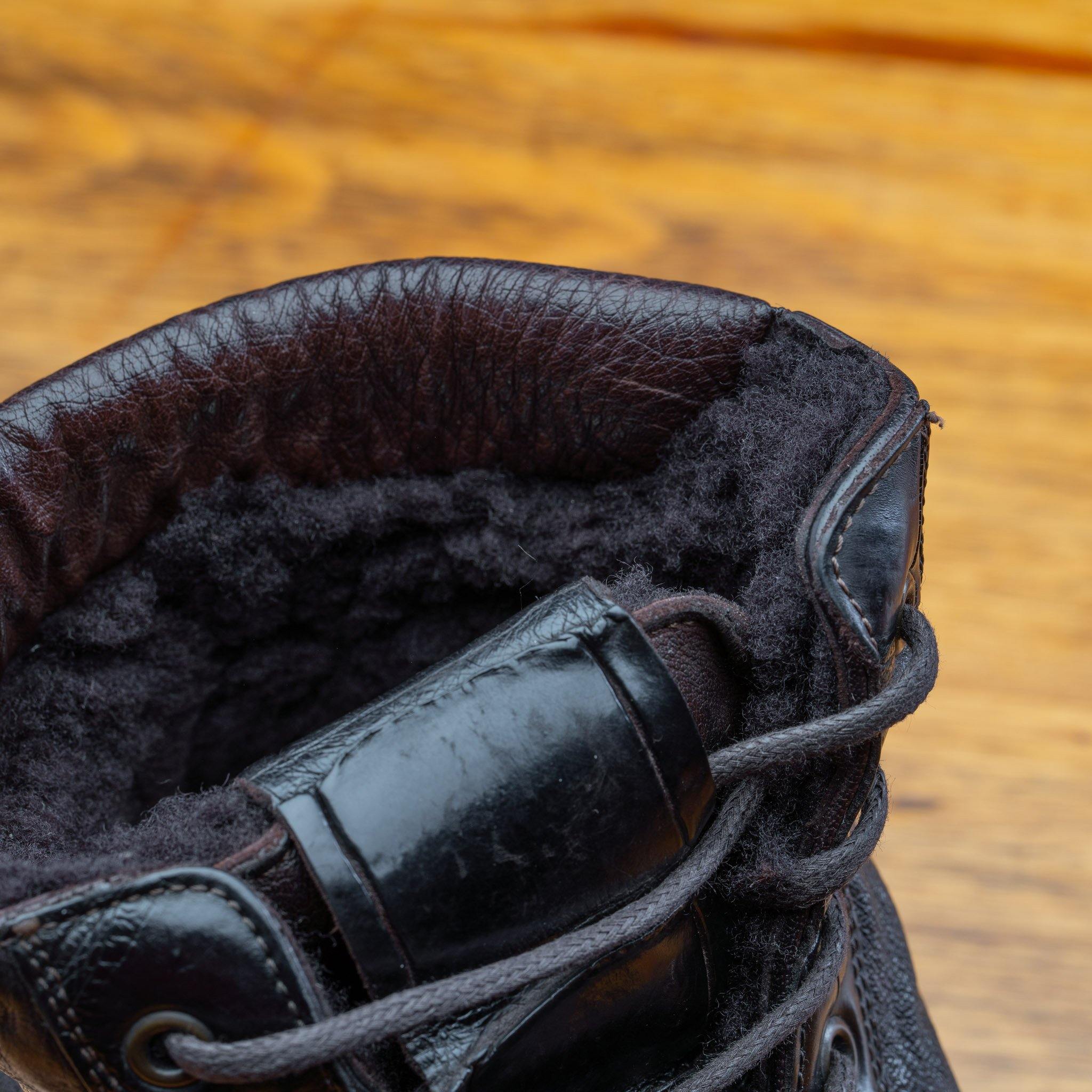 Close-up of a dark brown leather boot with shearling lining on a wooden surface.