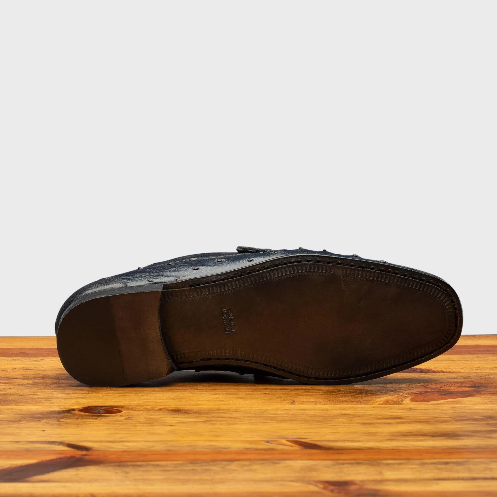 Outsole of Black leather loafer on a wooden surface with a light gray background
