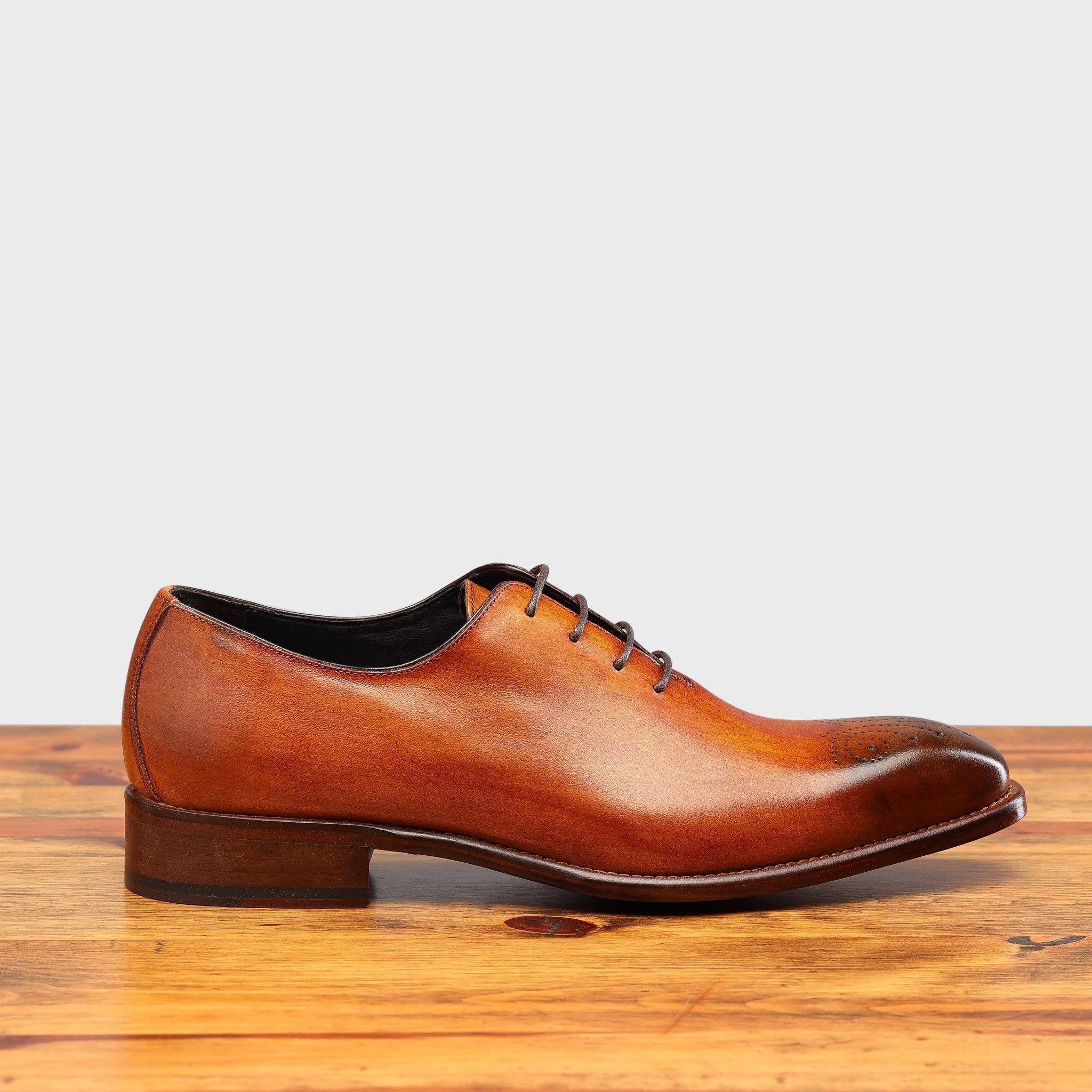 Caramel leather dress shoe on a wooden surface with a light gray background