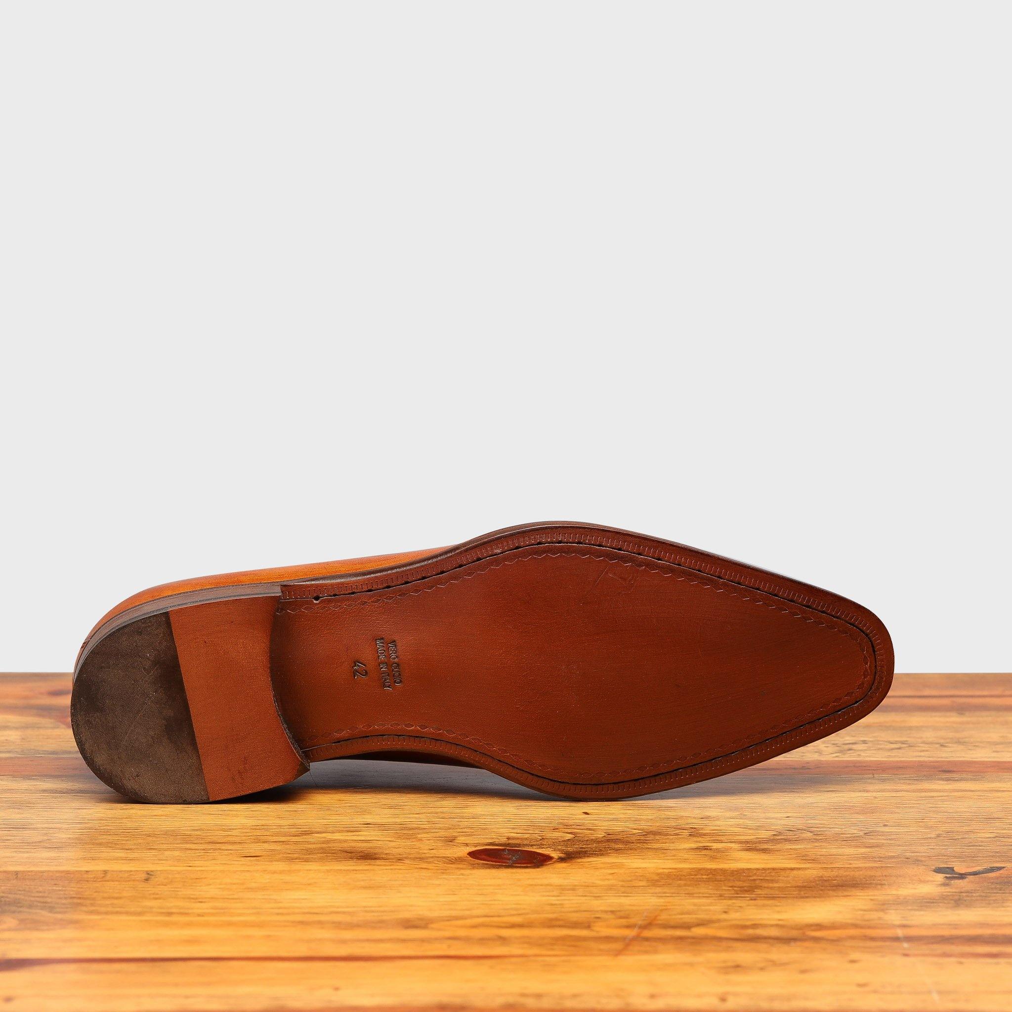 Outsole of Caramel leather dress shoe on a wooden surface with a light gray background