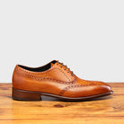 Brown leather dress shoe on a wooden surface with a light gray background