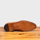 Outsole of Brown leather dress shoe on a wooden surface with a light gray background
