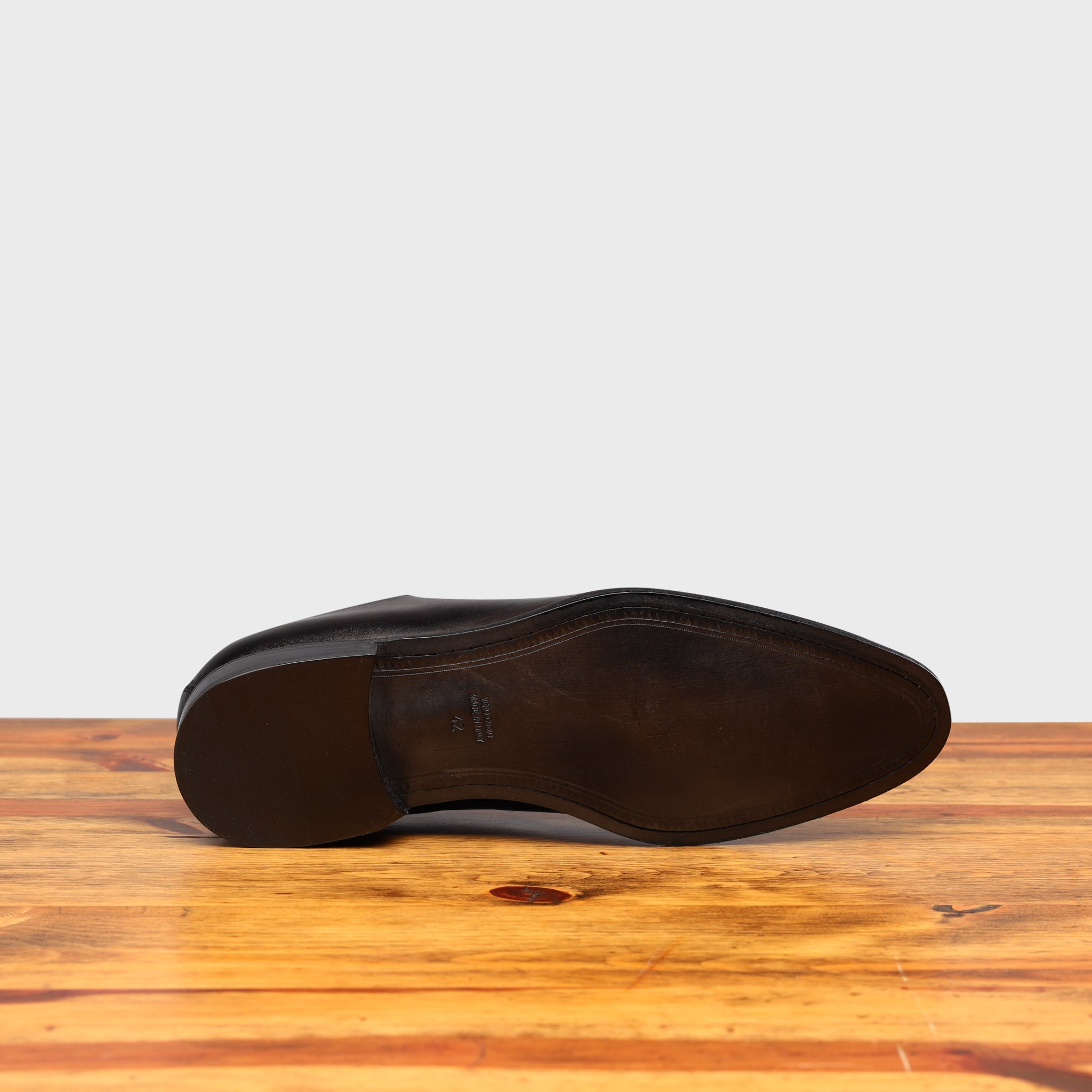 Outsole of Graphite leather dress shoe on a wooden surface with a light gray background