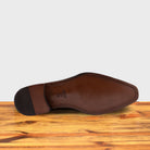 Outsole of a brown, wholecut blucher dress shoe with a lace-up closure, displayed on a wooden surface.