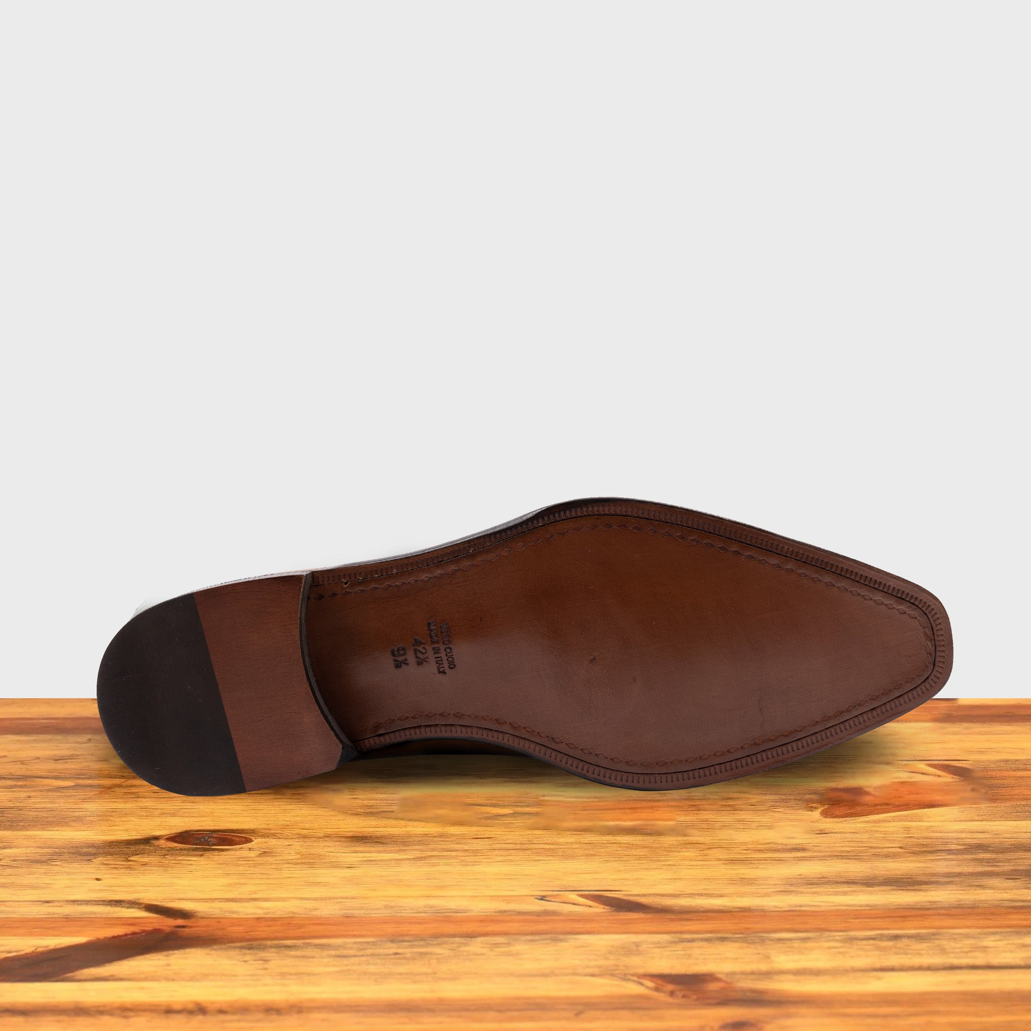 Outsole of a brown, wholecut blucher dress shoe with a lace-up closure, displayed on a wooden surface.