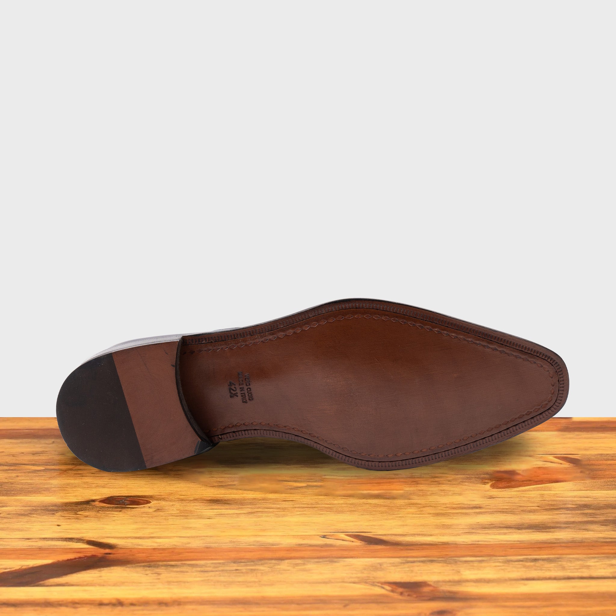 Outsole of Blue leather dress shoe on a wooden surface with a light gray background