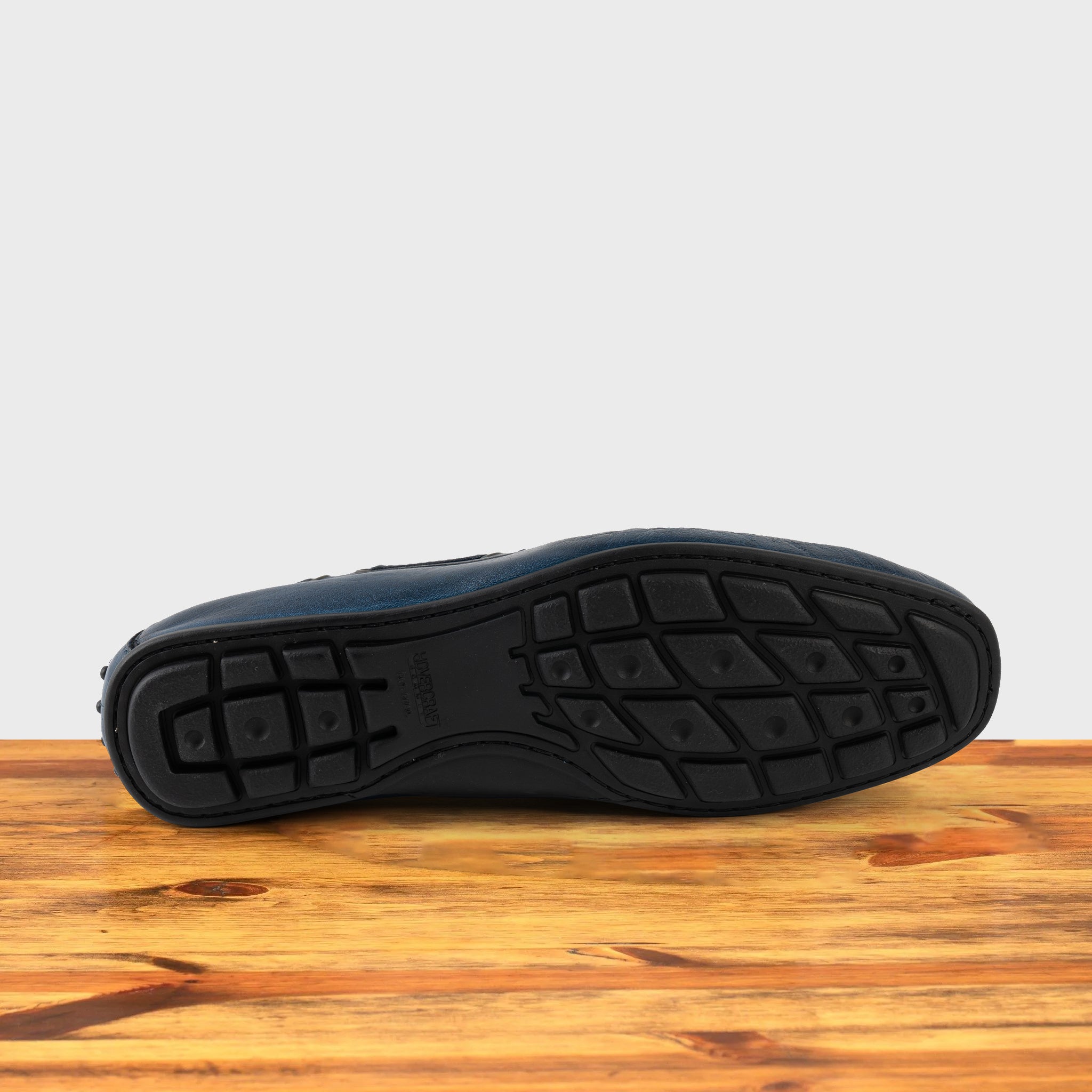 Outsole of Blue leather loafer on a wooden surface with a white background