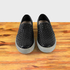 A Pair of black woven slip-on shoe on a wooden surface with a white background
