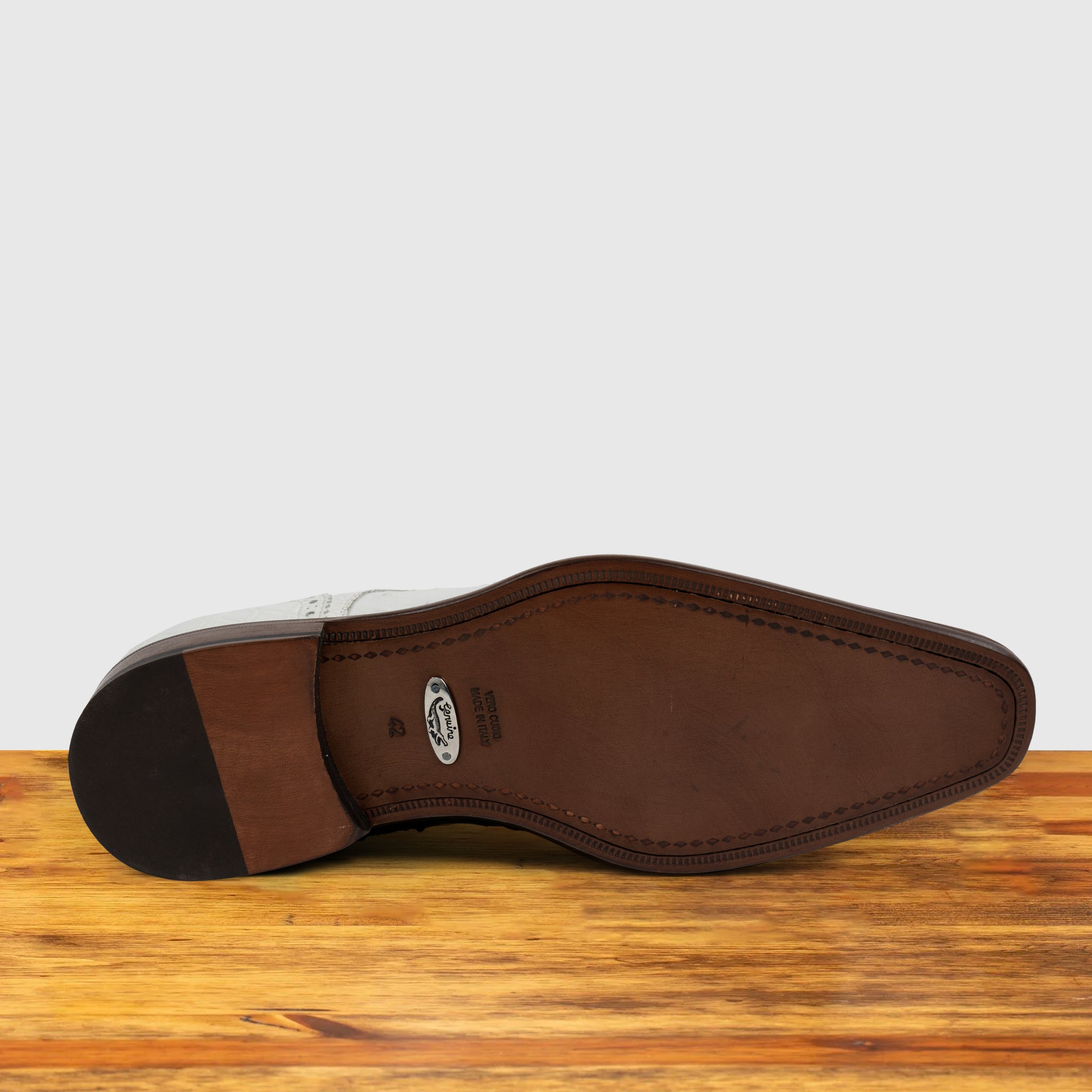 Outsole of white ostrich dress shoe with studded details on a wooden surface