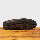 Outsole of Dark brown crocodile-patterned loafer on a wooden surface with a light gray background