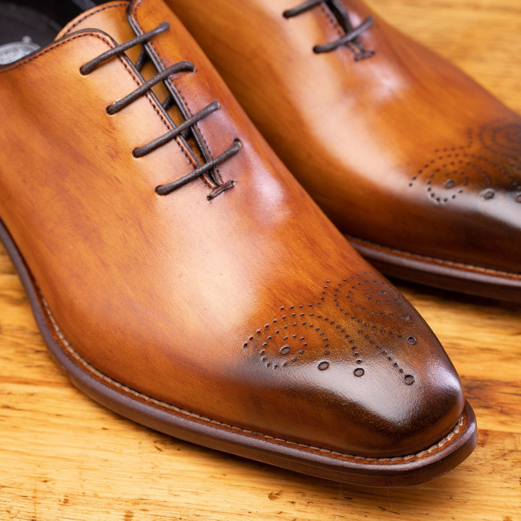 Caramel leather dress shoe on a wooden surface with a light gray background