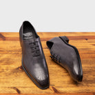 A Pair of Grey leather dress shoe on a wooden surface with a light gray background
