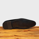 Outsole of Shiny blue dress shoe on a wooden surface with a light gray background