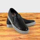 A Pair of black woven slip-on shoe on a wooden surface with a white background