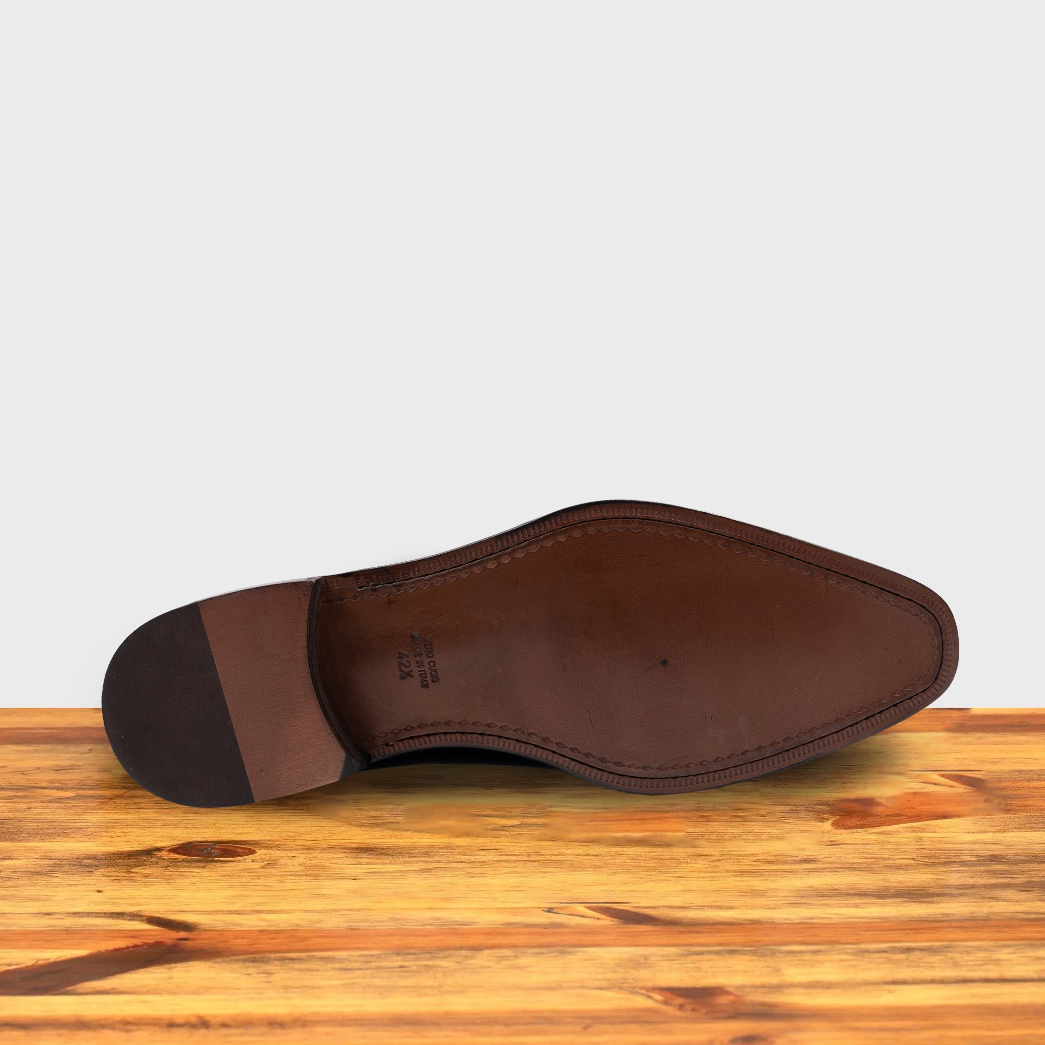 Outsolle of black wholecut blucher dress shoe with a lace-up closure, displayed on a wooden surface.