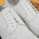 A Pair of white ostrich dress shoe with studded details on a wooden surface