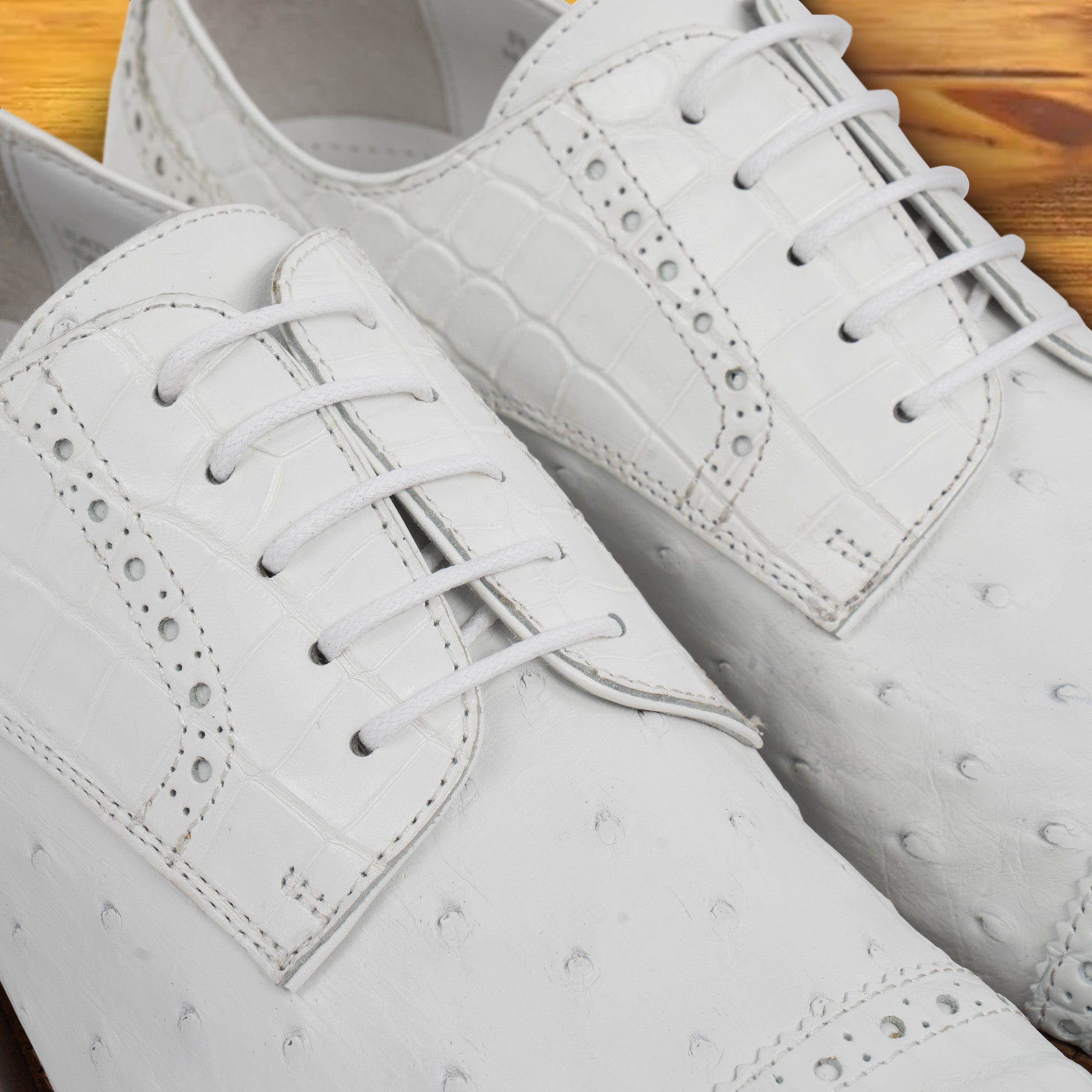 A Pair of white ostrich dress shoe with studded details on a wooden surface