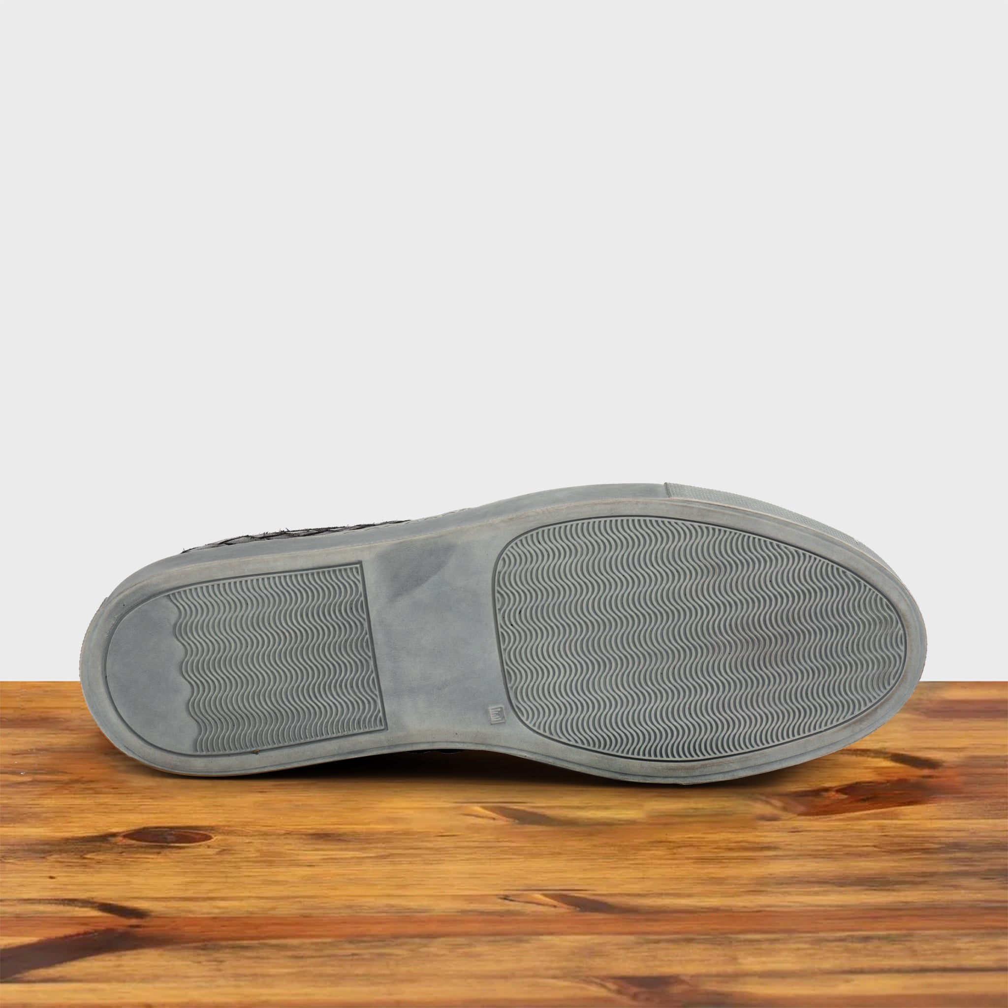 Outsole of Black woven sneaker on a wooden surface with a light gray background