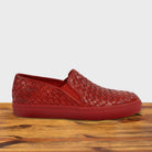Red woven slip-on shoe on a wooden surface with a white background