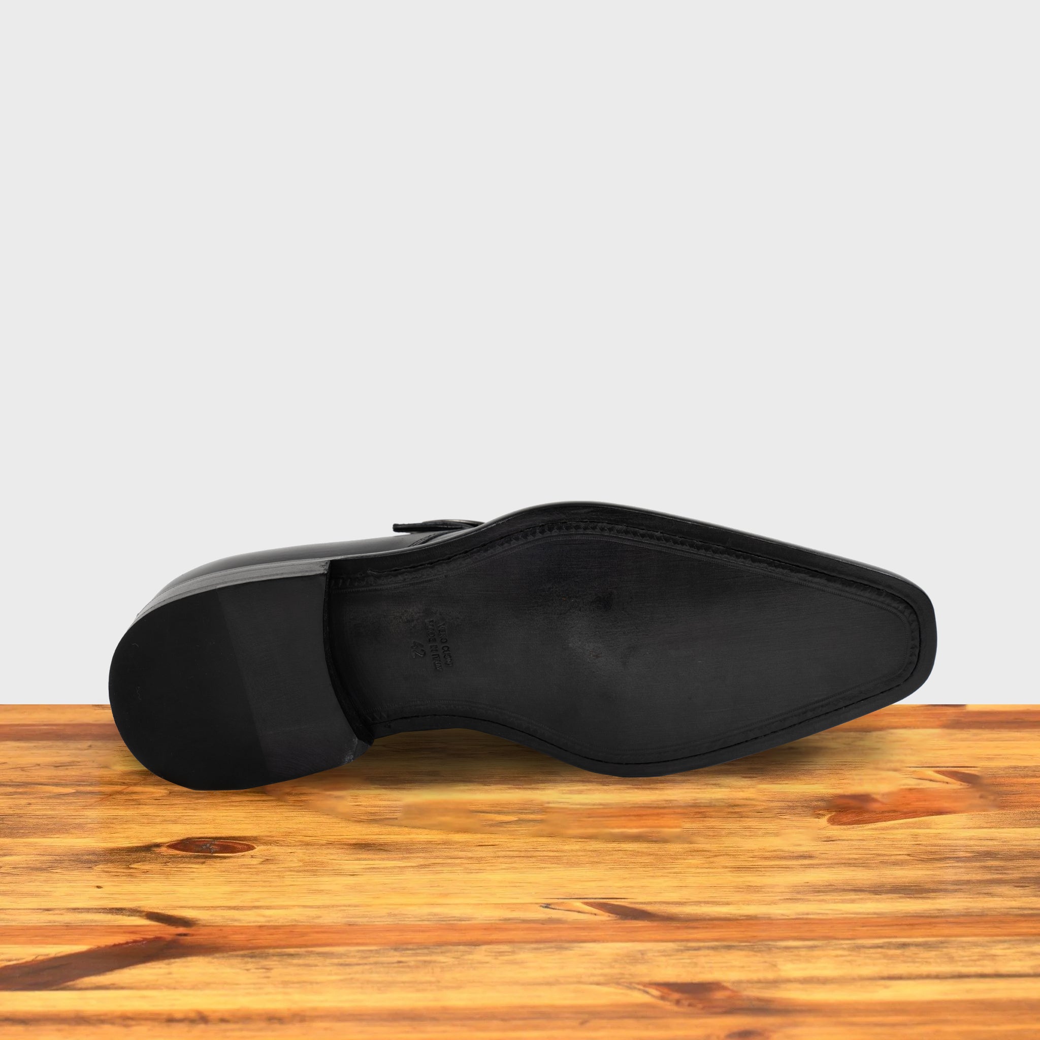 Outsole of a black monk strap shoe with a silver buckle on a wooden surface