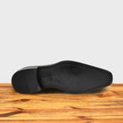 Outsole of Black leather shoe on a wooden surface with a light gray background