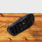Outsole of Black crocodile-patterned loafer on a wooden surface with a light gray background