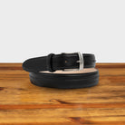 Black leather belt with silver buckle on a wooden surface