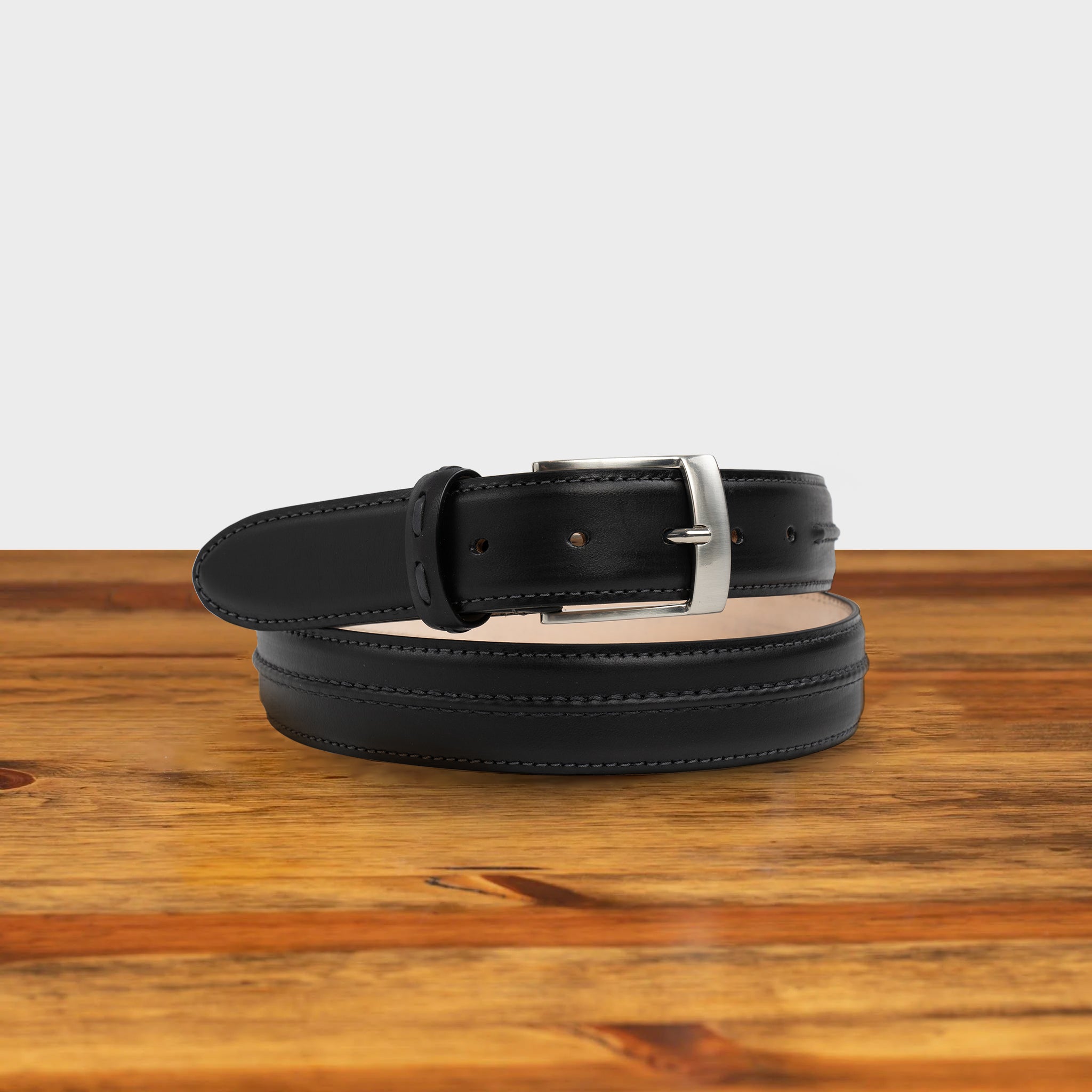 Black leather belt with silver buckle on a wooden surface