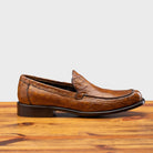 Brown leather loafer on a wooden surface with a light gray background