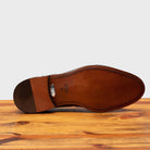 Outsole of Brown leather loafer on a wooden surface with a light gray background