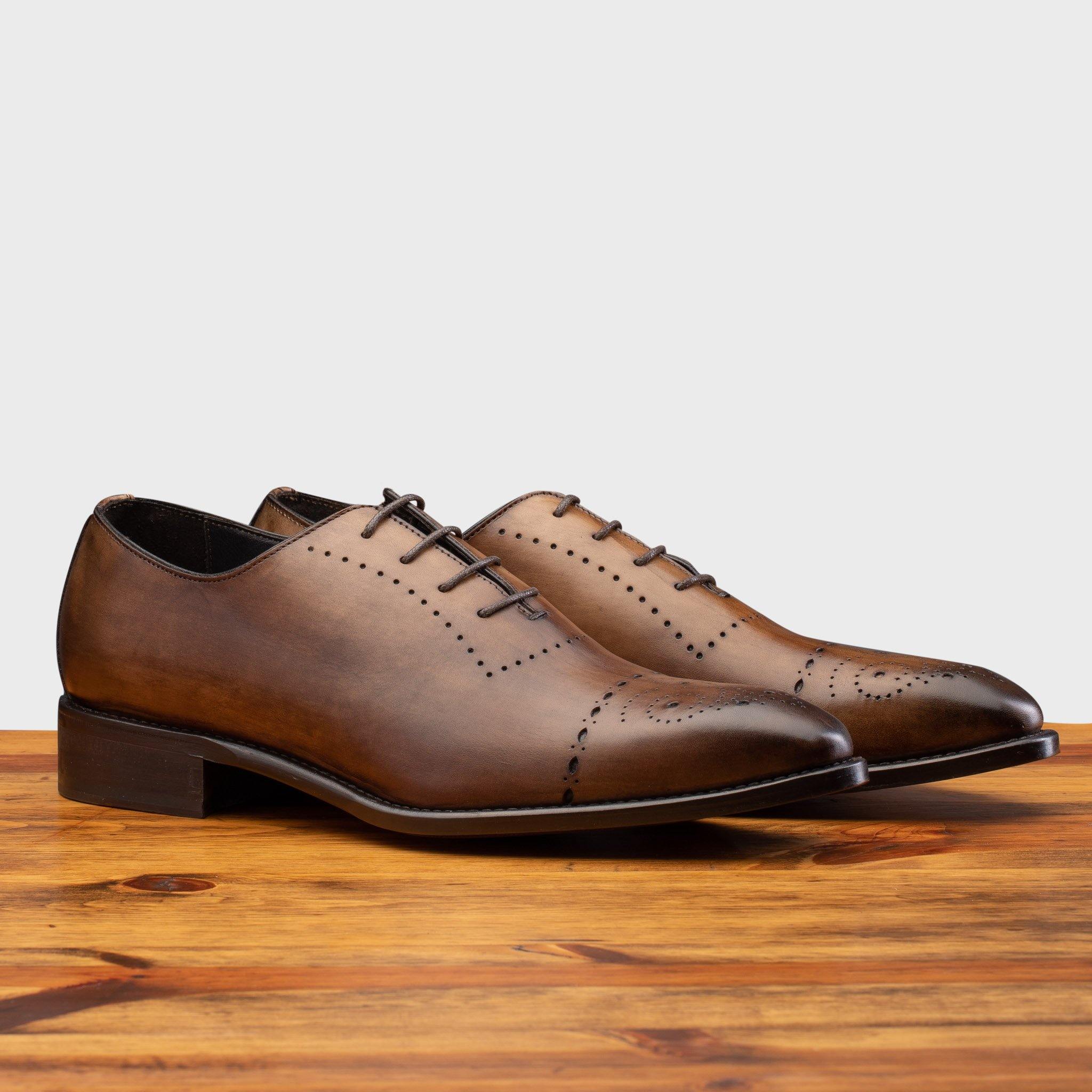 A Pair of Brown leather dress shoe on a wooden surface with a light gray background