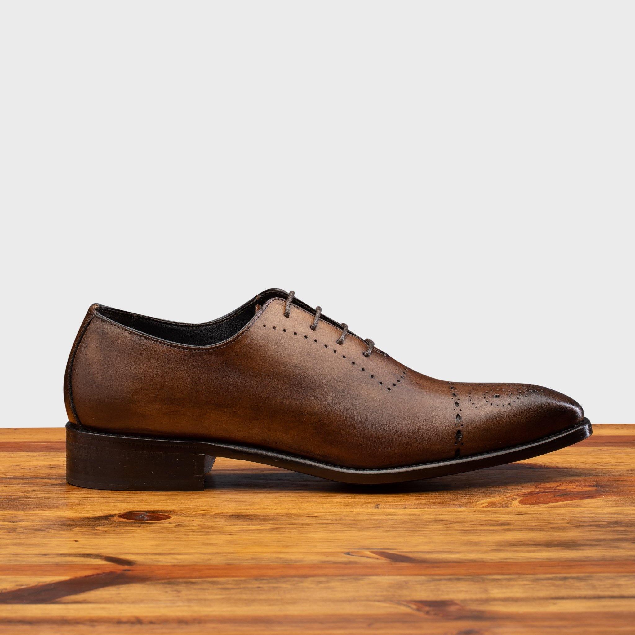 Brown leather dress shoe on a wooden surface with a light gray background