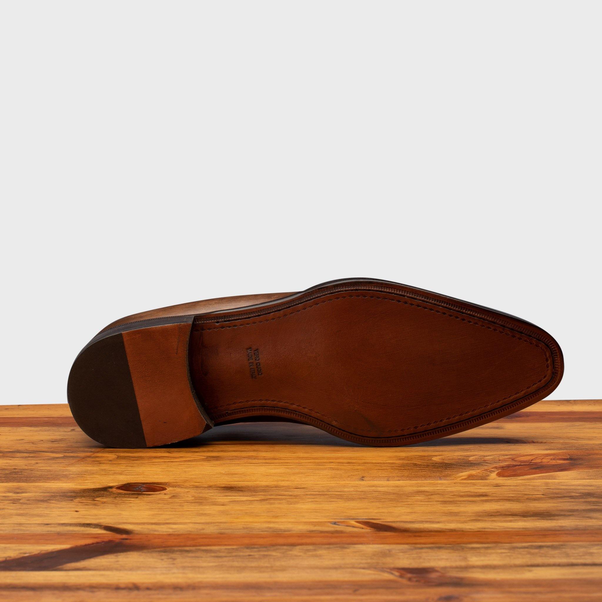 Outsole of Brown leather dress shoe on a wooden surface with a light gray background