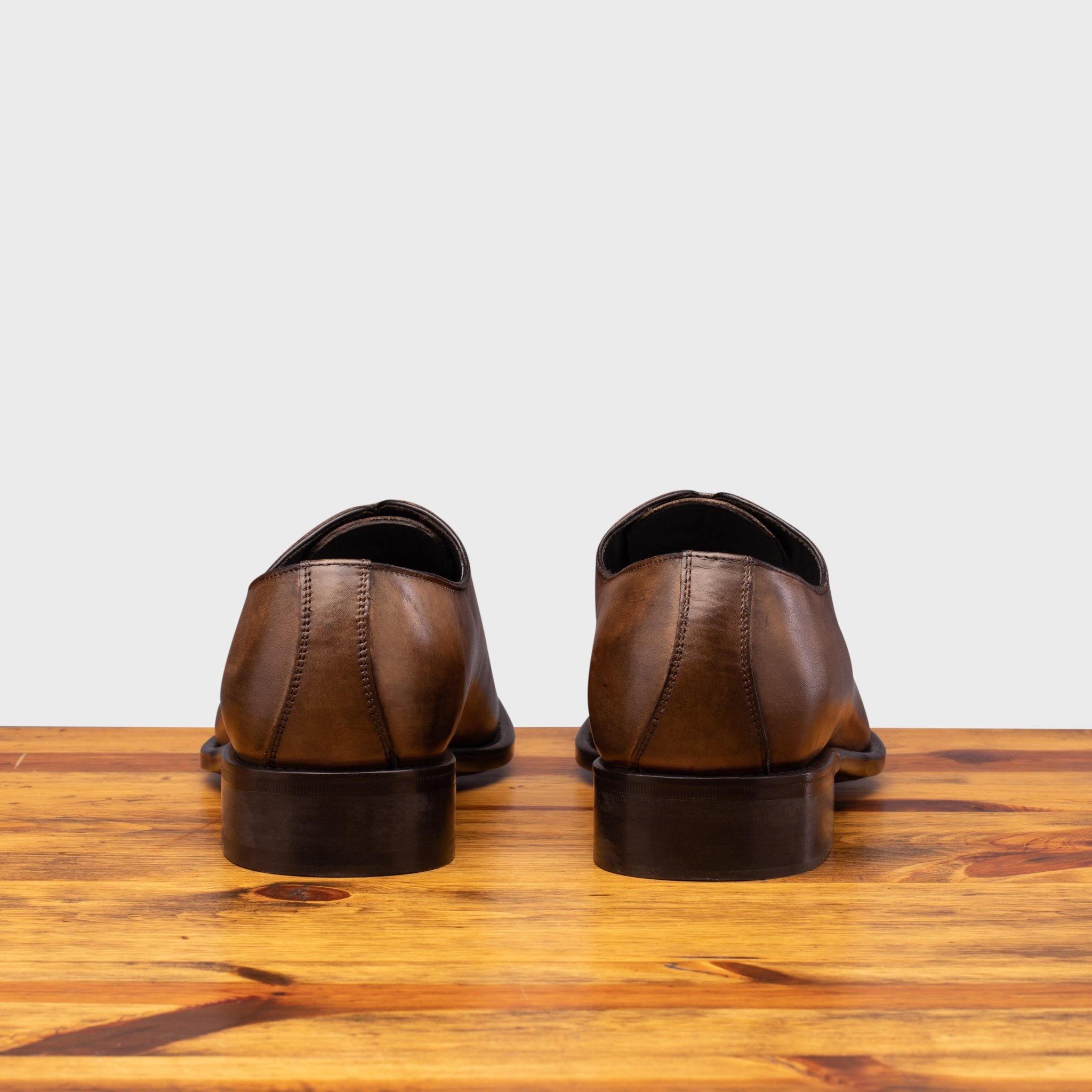 Brown leather dress shoes on a wooden surface with a light gray background