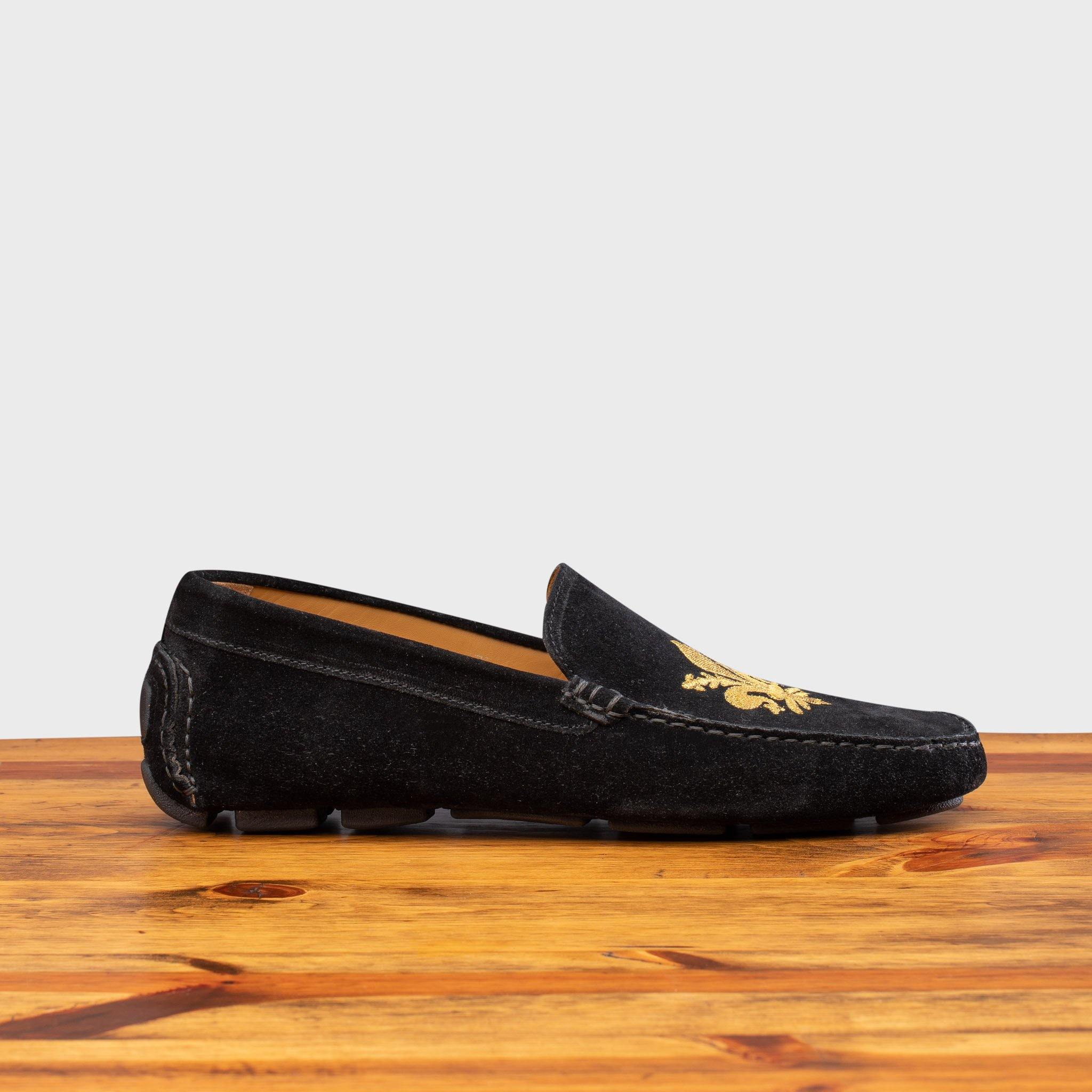 Black loafer with gold embroidery on a wooden surface