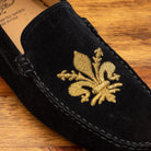 Black loafer with gold embroidery on a wooden surface
